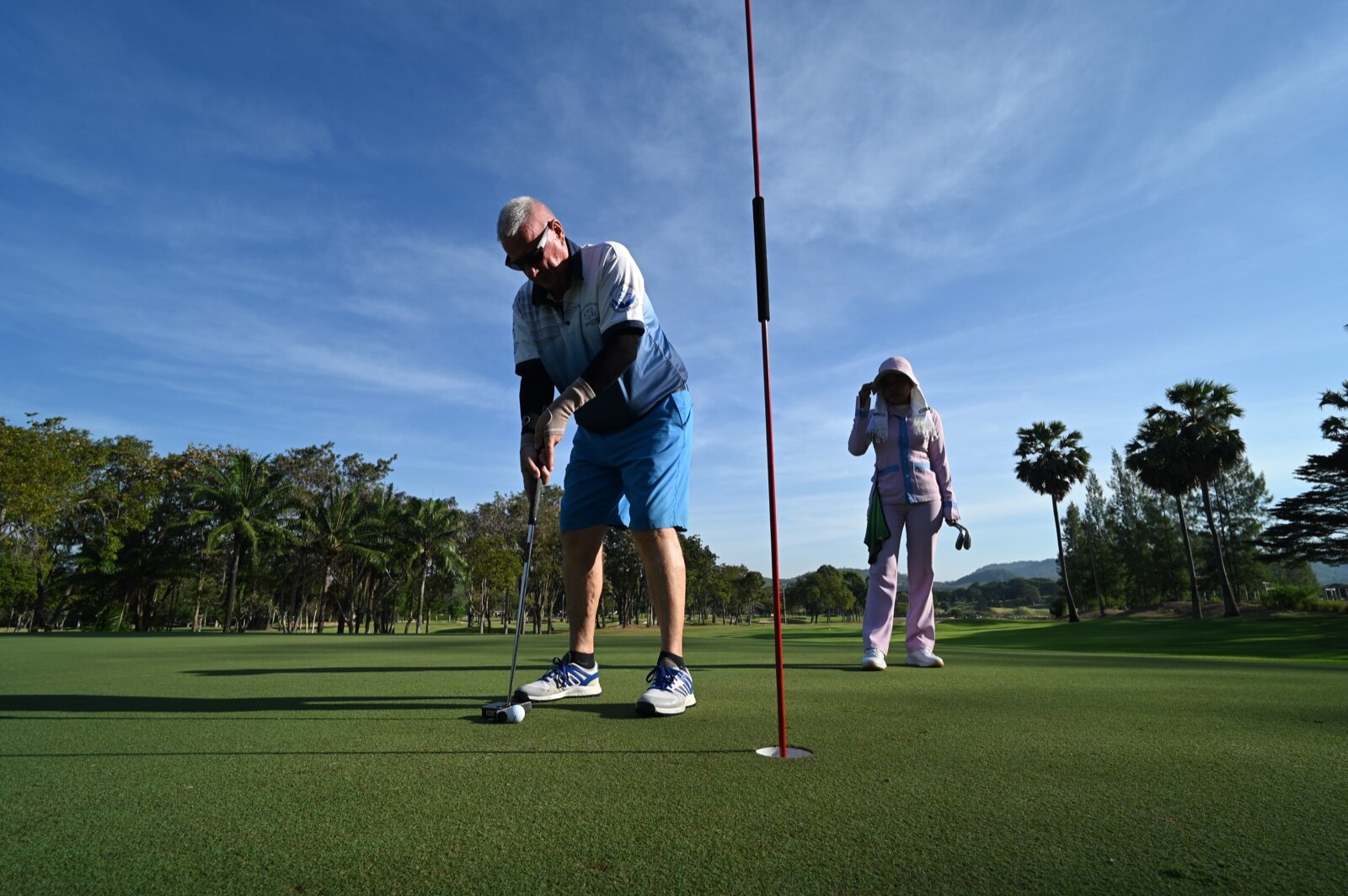 Two golfers on a putting green, one lining up a putt beside the flagstick