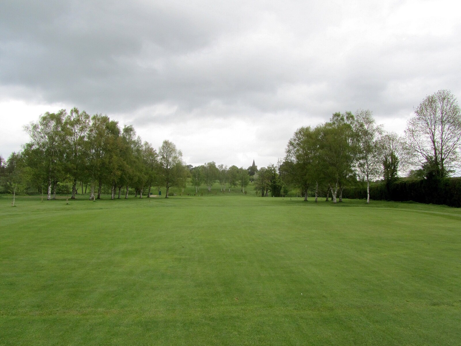 A tree-lined fairway on a Kent parkland golf course, with a church spire in the distance