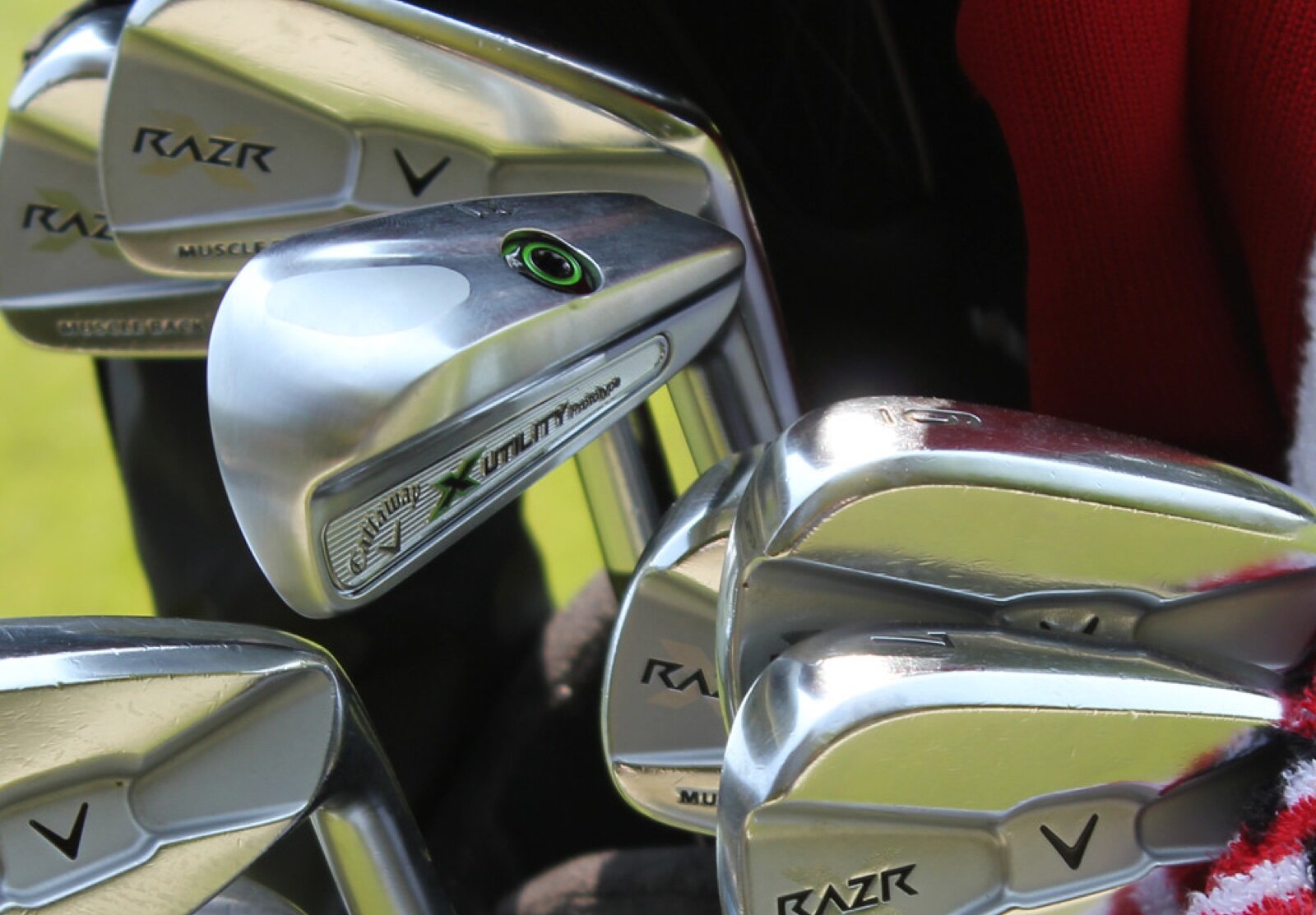 A close-up of a set of chrome cavity back golf irons standing in a bag alongside a utility iron