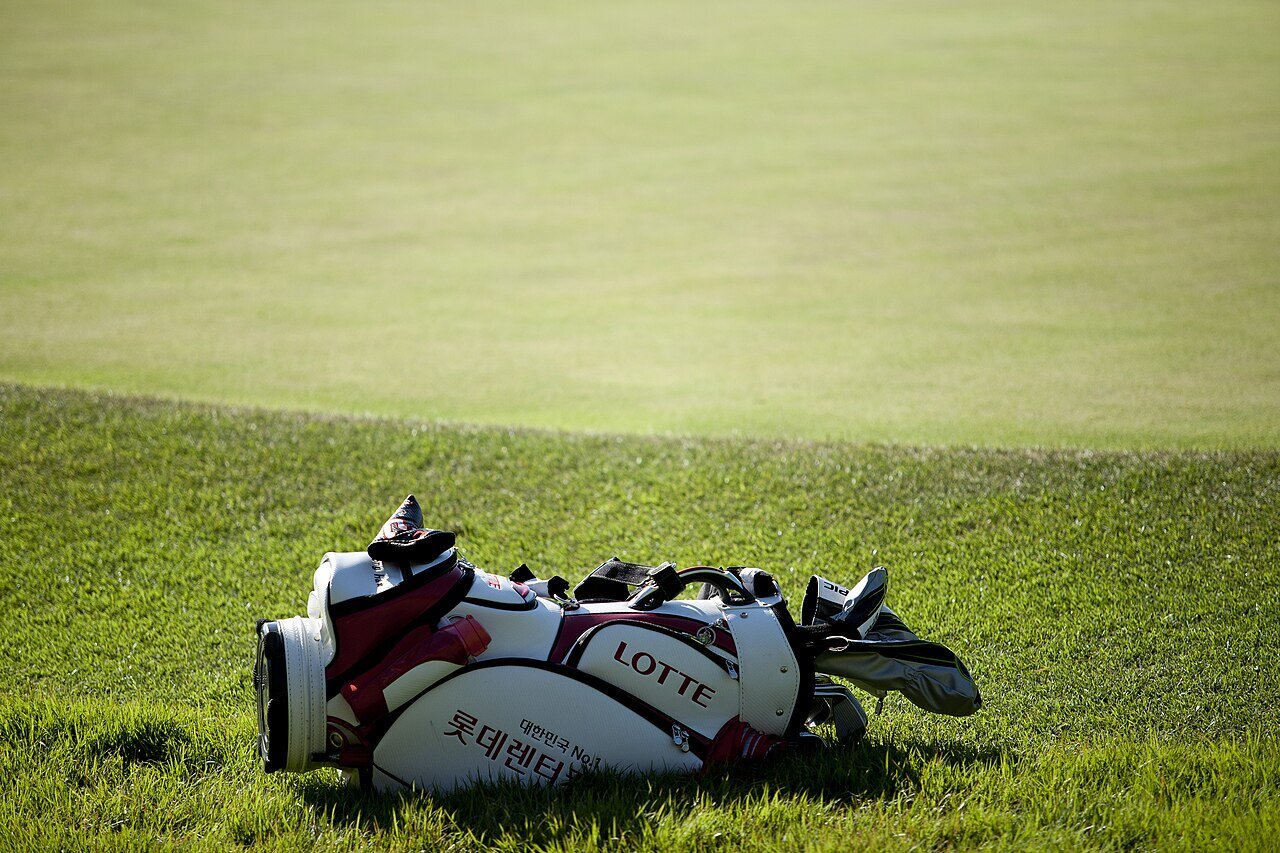 A large white and red tour-style golf bag lying on the grass beside a green