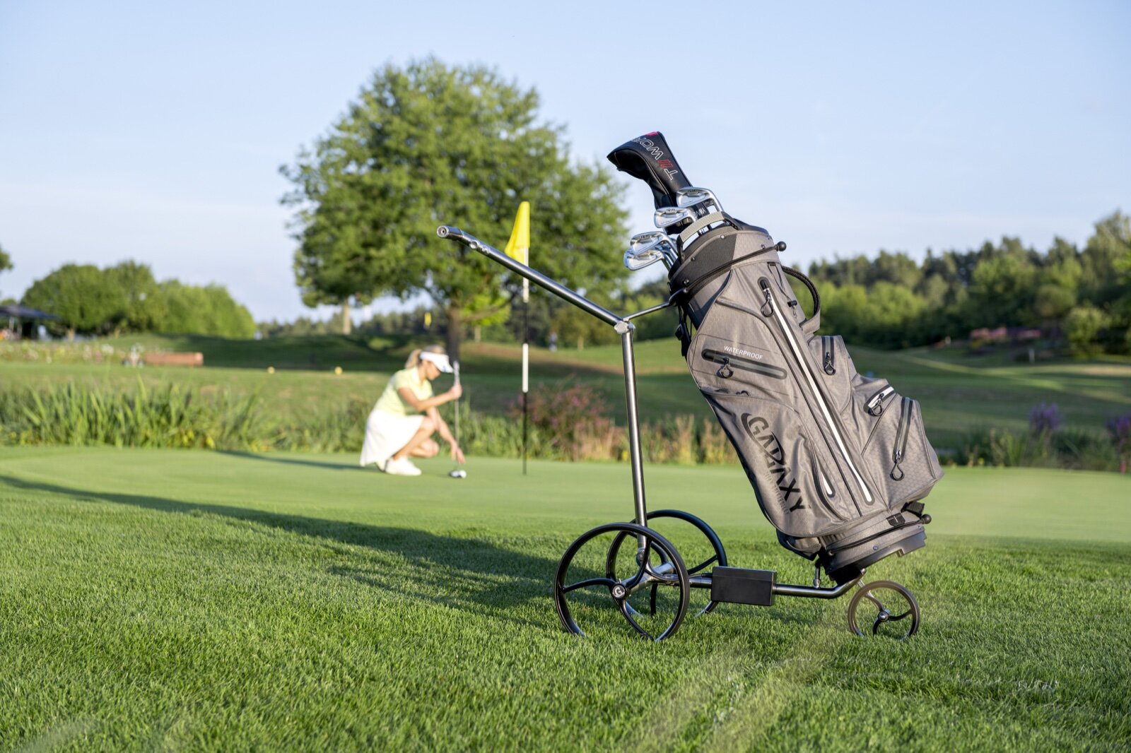 An electric golf trolley carrying a bag on a green, with a flag behind